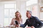 Mature couple using smart phone at breakfast table