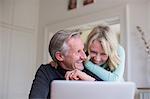 Laughing, carefree mature couple using laptop