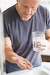 Mature man taking vitamins with glass of water