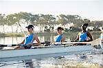 Female rowing team rowing scull on sunny lake