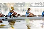 Female rowing team rowing scull on sunny lake