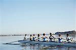 Female rowers rowing scull on sunny lake under blue sky