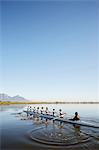 Female rowers rowing scull on tranquil lake under blue sky