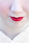 Close up of Geisha's face with traditional make up, pale white skin and bright pink lipstick.