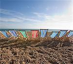 Row of striped beach chairs on a pebble beach by the ocean.