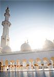 Exterior view of mosque with white washed walls and colonnade, minaret and domes.