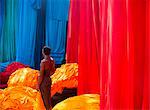 High angle view of person standing in between bright and vibrant heaps of blue, red and orange fabric.