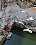 High angle view of two women wearing pink saris walking up stairwell around water pool of an ancient building.