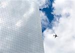 Low angle view of glass facade of contemporary skyscraper, passenger plane in cloudy sky.