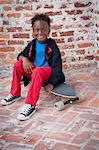 Portrait of young boy sitting on skateboard, smiling