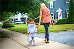 Mid adult woman walking with daughter on suburban sidewalk, rear view