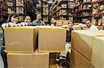 Team portrait of multi-ethnic male and female warehouse workers in a large distribution warehouse full of products stored on pallets in cardboard boxes on large racks.