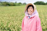 Smiling woman wearing straw hat and pink jacket standing in a rice field, looking at camera.