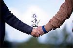 Close up of elderly man and woman standing outdoors, holding hands.