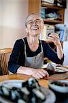 Elderly woman sitting at kitchen table, eating sushi, smiling at camera.