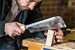 Close up of man working standing in a woodworking workshop, using saw on piece of wood.