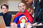 A middle aged Caucasian office super hero in a meeting with his staff.