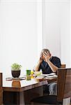Hispanic man under stress while sitting at the dining room table in a new home.