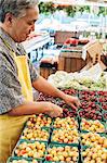 Man wearing apron standing at stall with punnets of fresh cherries at a fruit and vegetable market.