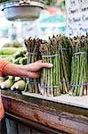 Close up of human hand holding bunch of fresh green asparagus at a fruit and vegetable market.