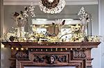 Close up of Christmas decorations on beautifully carved wooden mantelpiece, mirror above.