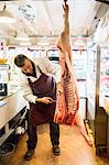 Man wearing apron standing in butcher shop, butchering half a pig.