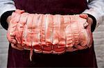 Close up of butcher wearing apron holding large rolled pork belly.