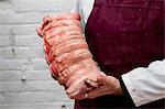 Close up of butcher wearing apron holding large rolled pork belly.