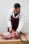 Man wearing apron standing at a wooden butcher's block, butchering piece of pork loin.