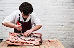 Man wearing apron standing at a wooden butcher's block, butchering beef forerib.