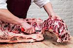 Close up of butcher wearing apron standing at a wooden butcher's block, butchering beef forerib.