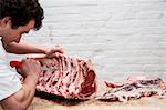 Close up of man wearing apron standing at a wooden butcher's block, butchering beef forerib.