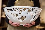 Close up of potter wearing apron holding a large intricate white ceramic bowl.