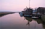 Sailing boats moored at harbour wall, reflected on the surface of a calm canal at twilight.