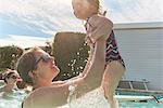 Woman holding toddler daughter up in swimming pool