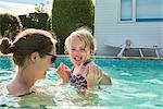 Woman holding toddler daughter hands in swimming pool