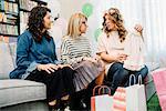 Pregnant woman and friends on sofa looking at baby dress