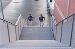 Young adult male twins running together, running up city stairway