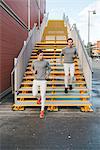 Young adult male twins running together, running down city stairway