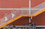 Young adult male twins running together, running up city stairs