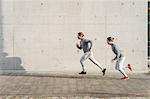 Young adult male twins running together, running up sidewalk
