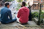 Three mature men, outdoors, sitting on steps, playing cards, rear view