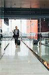 Woman walking, pulling wheeled suitcase, holding smartphone