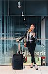 Portrait of woman standing beside wheeled suitcase, holding smartphone