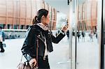 Woman outdoors, using smartphone, carrying luggage