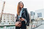 Businesswoman walking outdoors, holding smartphone, smiling