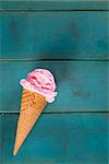 Top view strawberry ice cream waffle cone on blue wooden background, close up.