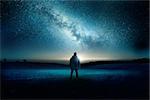 A man stands watching with wonder and amazement as the moon and milky way galaxy fill the night sky. Night time landscape. Photo composite.