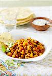 Bowl of chickpea curry with papadum and raita