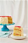 Vanilla rhubarb layer cake on a turquoise cake stand with a piece taken out and served on a dessert plate with fork on a white background